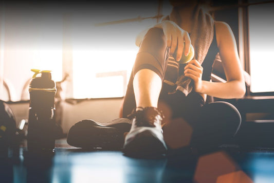 A woman sits on the floor of a gym with her water bottle, recovering from a workout